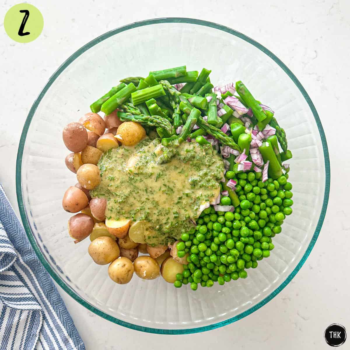Large glass bowl with mini potatoes, peas, asparagus, red onion and lemon Dijon dressing inside.