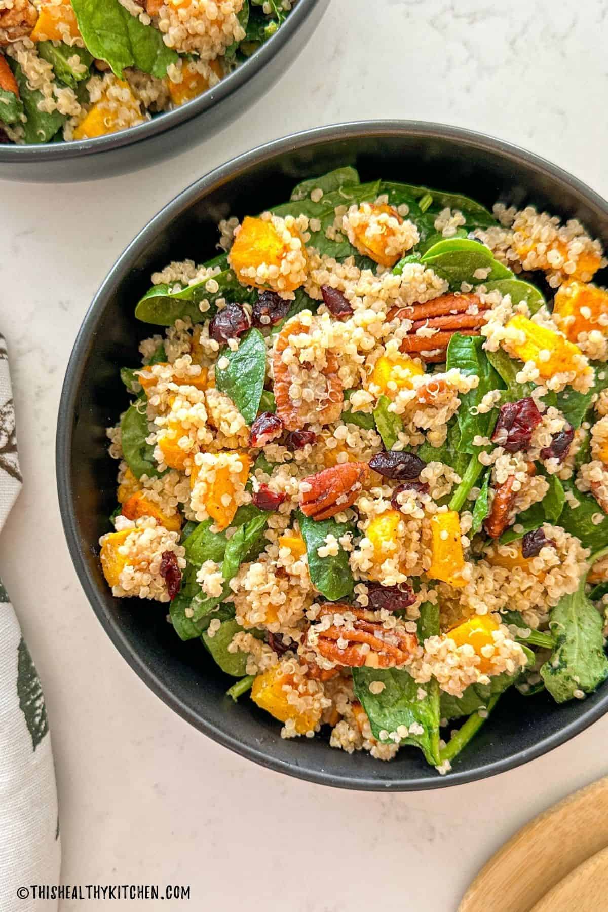 Black bowl with pumpkin quinoa salad inside topped with cranberries and pecans.