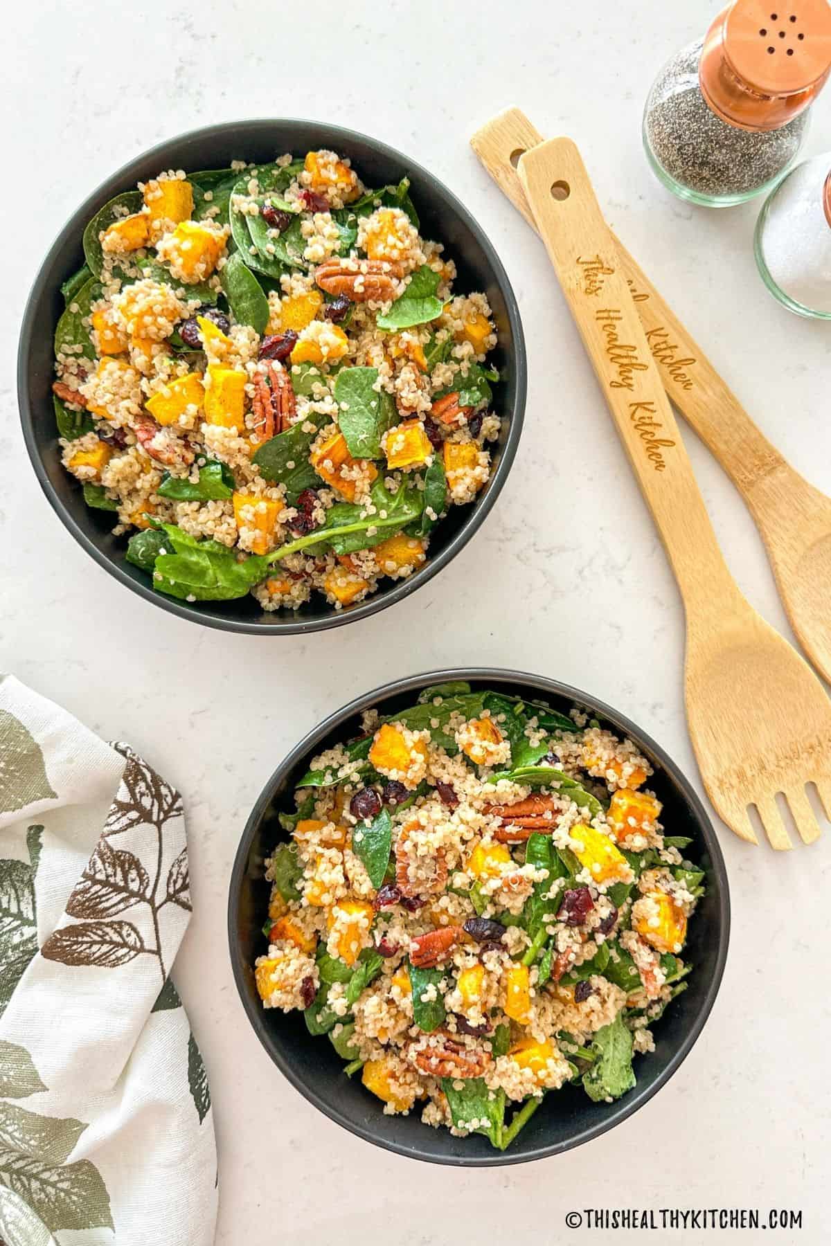 Two bowls of quinoa and spinach salad with roasted pumpkin, pecans and cranberries.