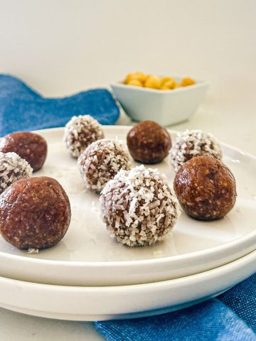 Bliss balls on white plate with bowl of macadamia nuts in the background.