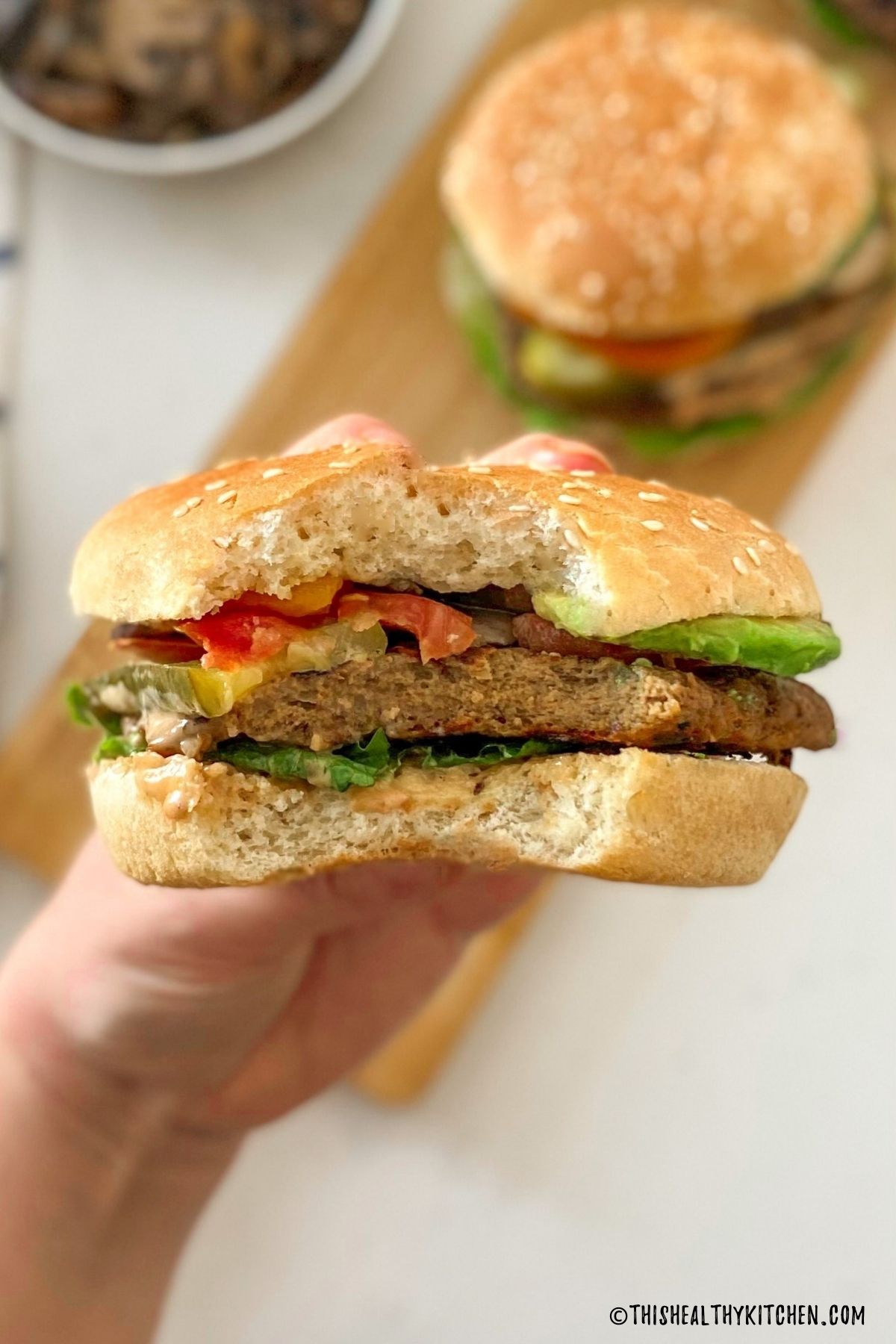 Hand holding up burger with bite taken out of it.