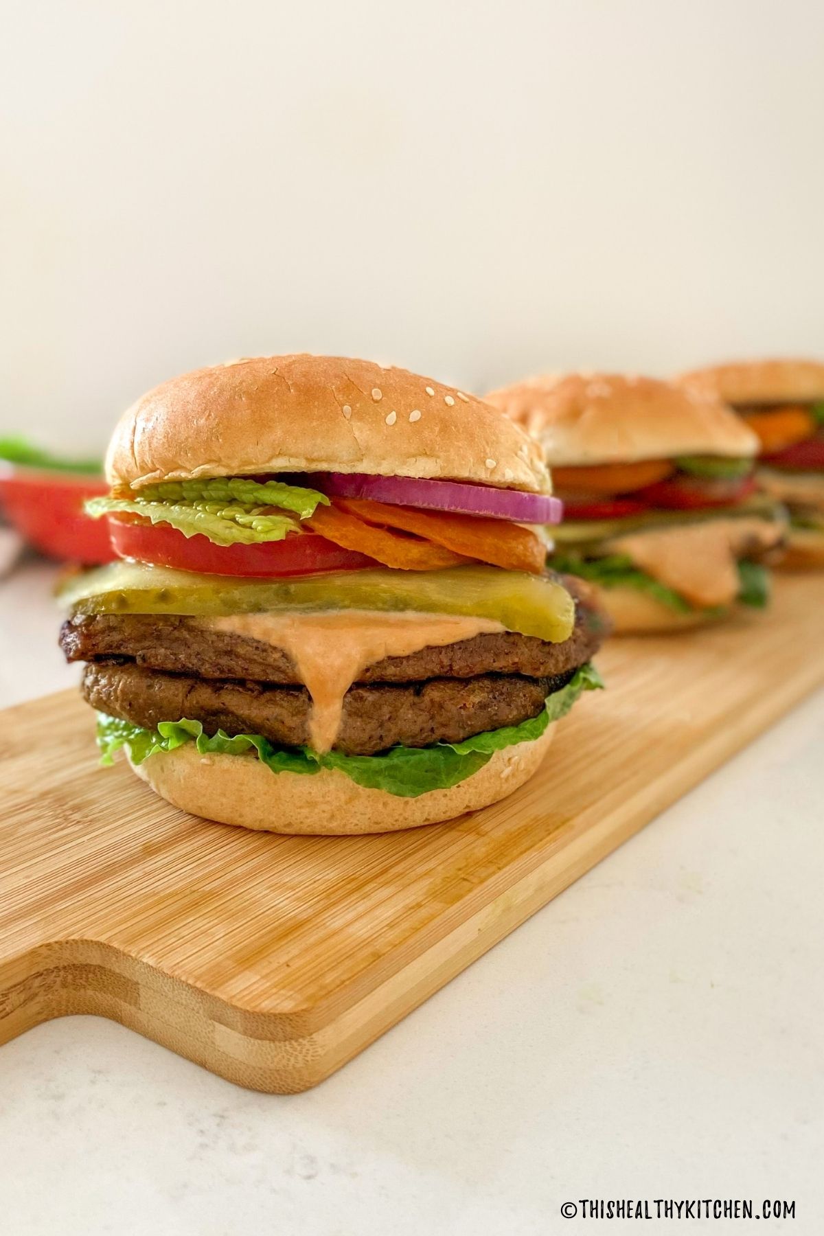 Seitan burger with double stacked patties, lettuce, tomato, pickle, onion, and spicy mayo.