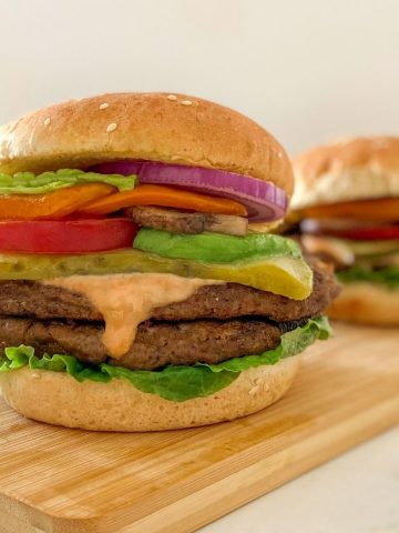 vegan burger in bun with tomato, lettuce, pickle, onion and spicy mayo.