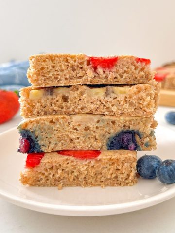 Side view of stack of 4 square slices of sheet pan pancakes studded with fruit.