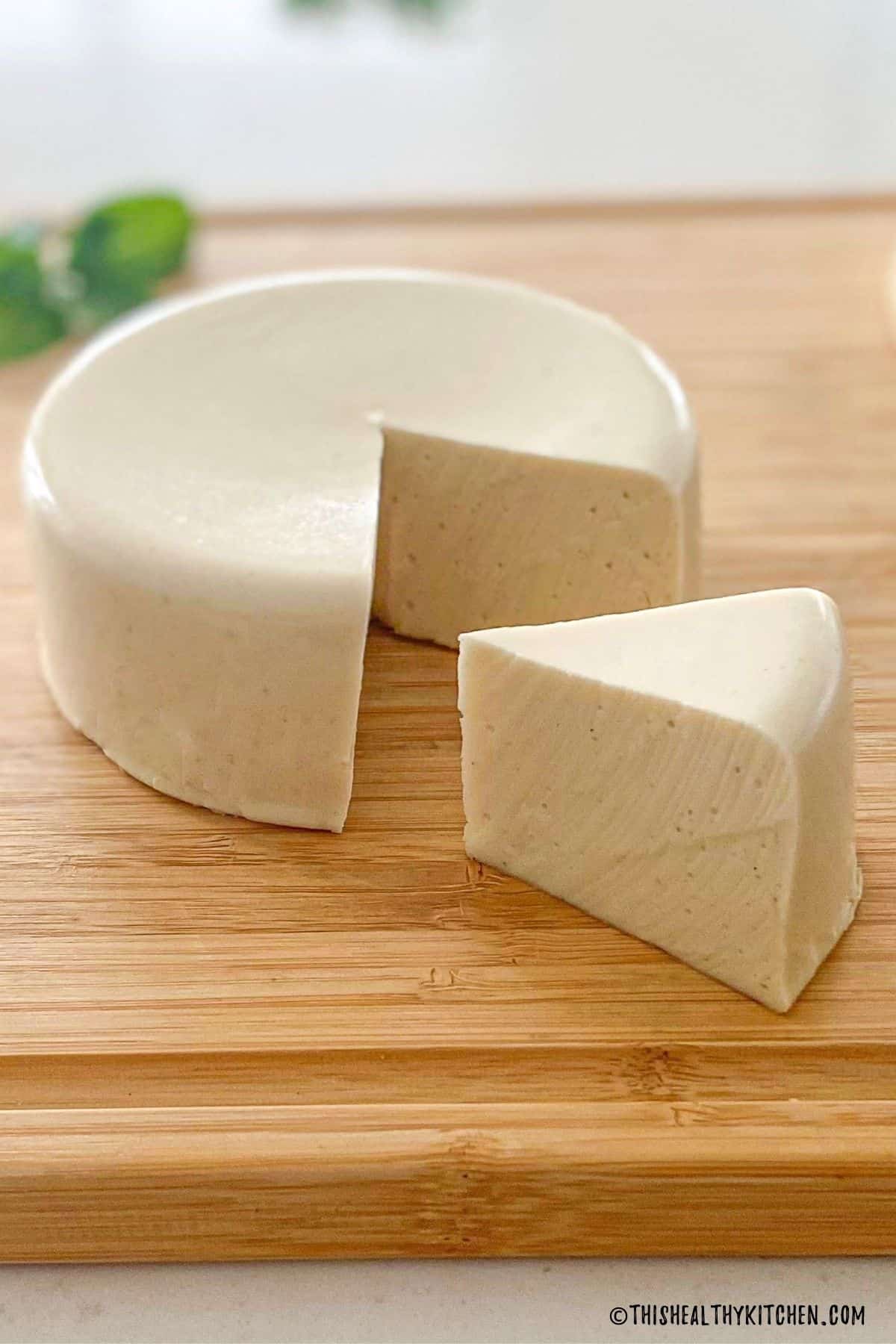 Round cheese block on cutting board with triangular wedge cut out.