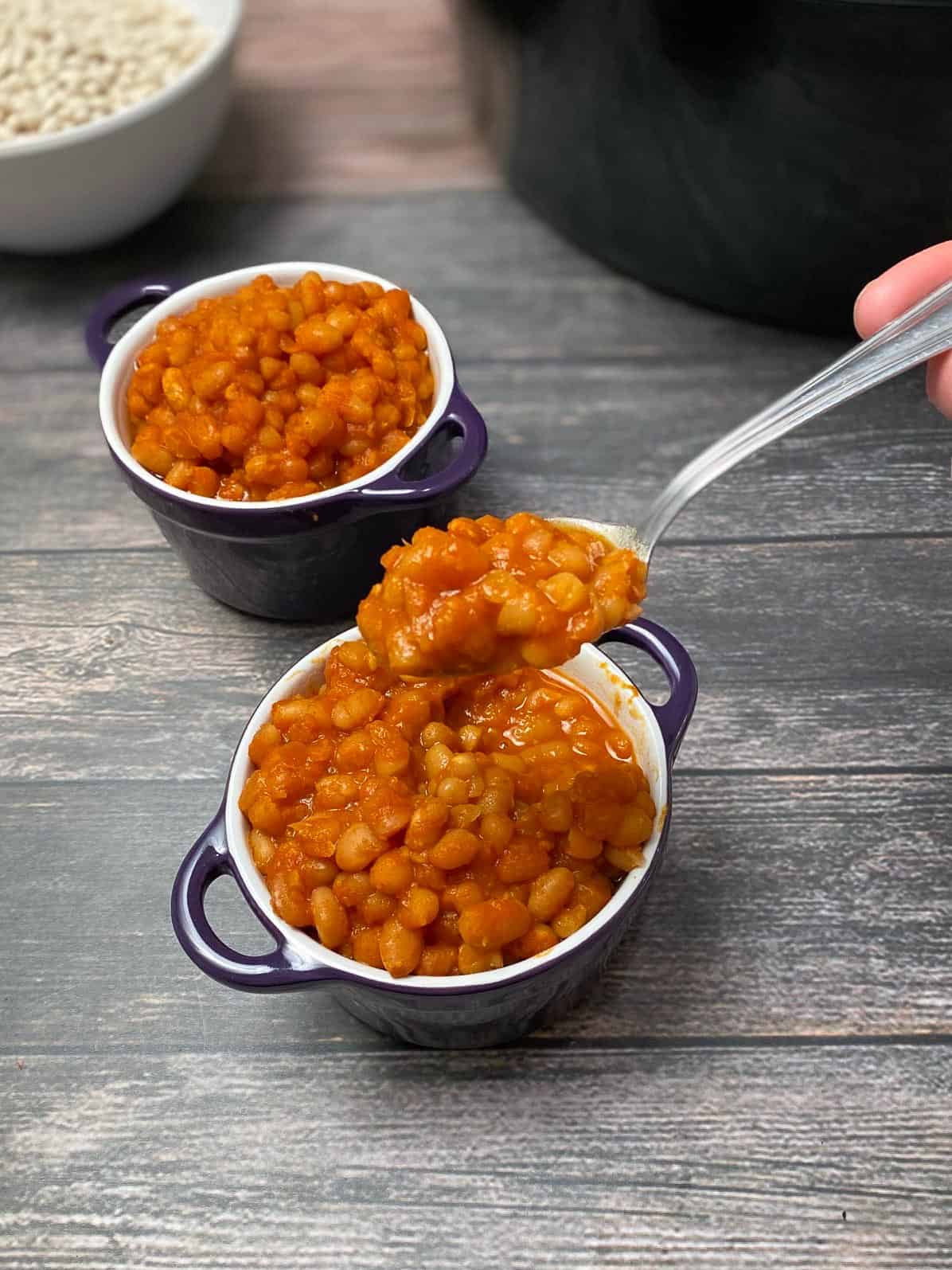 spoon picking up bite of baked beans from purple bowl