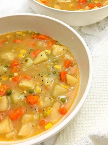 two bowls of vegetable soup with white dish towel beside them.