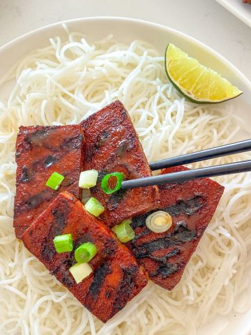 Chopsticks grabbing a piece of tofu from plate.