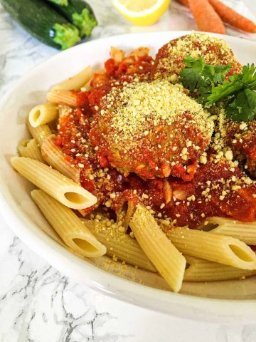 pasta and zucchini meatballs in plate with cashew cheese sprinkled on top