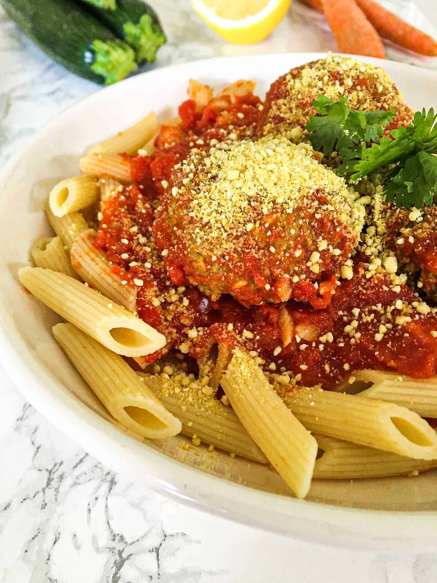 pasta and zucchini meatballs in plate with cashew cheese sprinkled on top