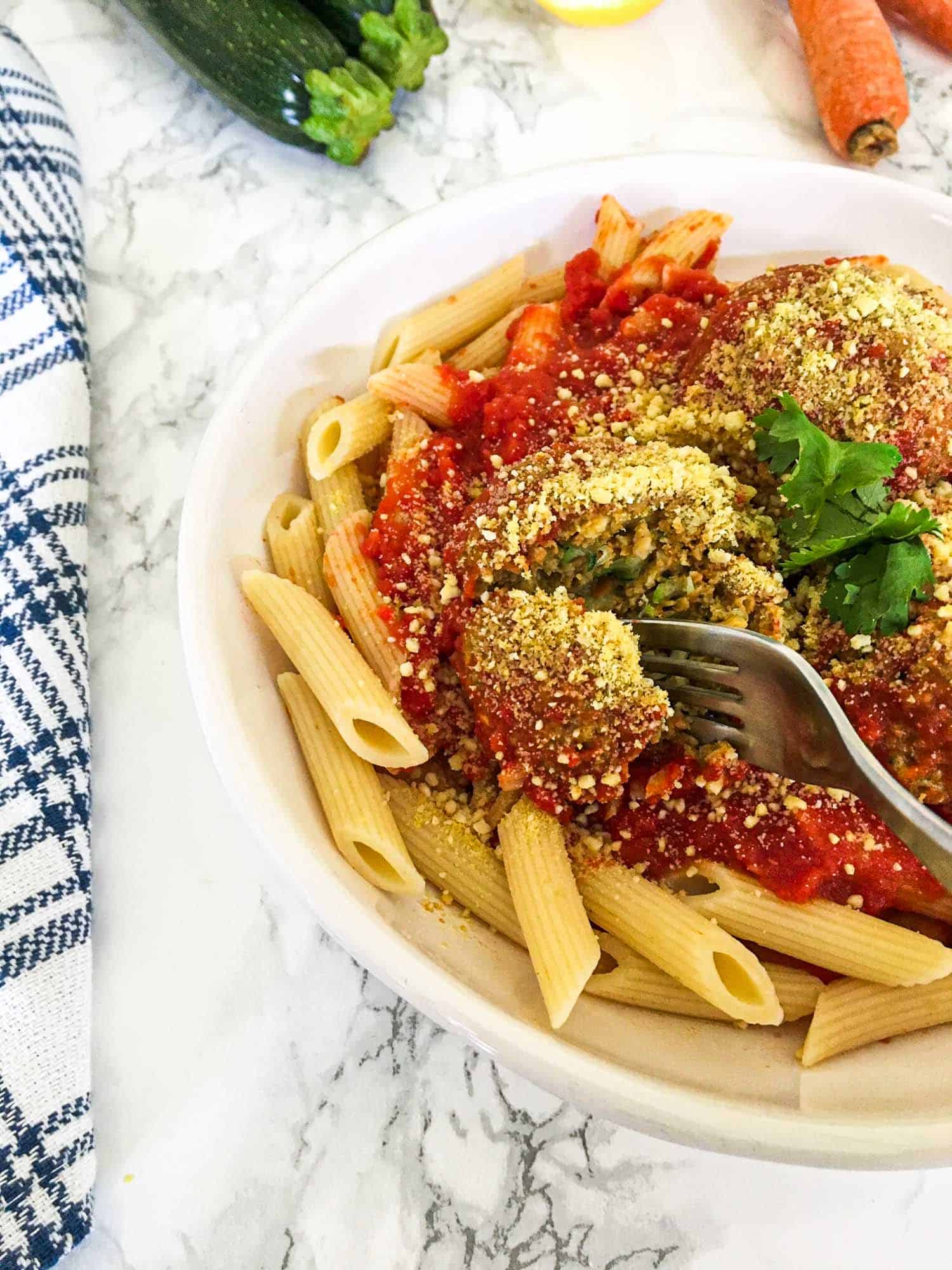 fork cutting through vegan meatball on bed of pasta