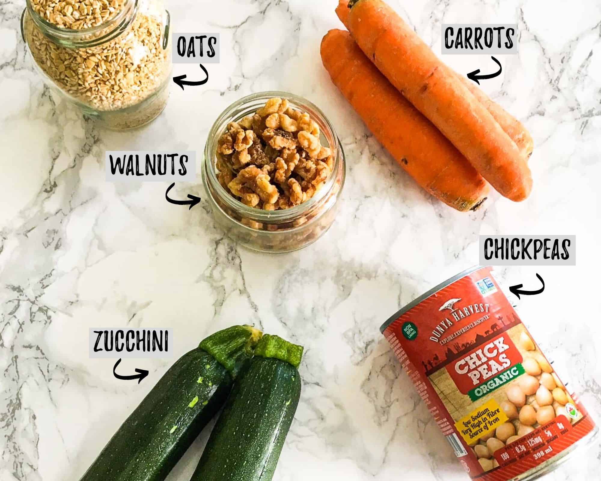 carrots, zucchini, can of chickpeas, jar of walnuts and jar of oats on marble counter