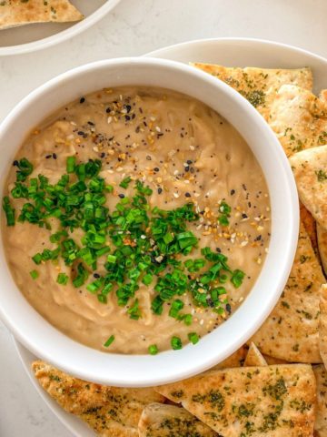 Bowl of vegan onion dip with pita chips around it.