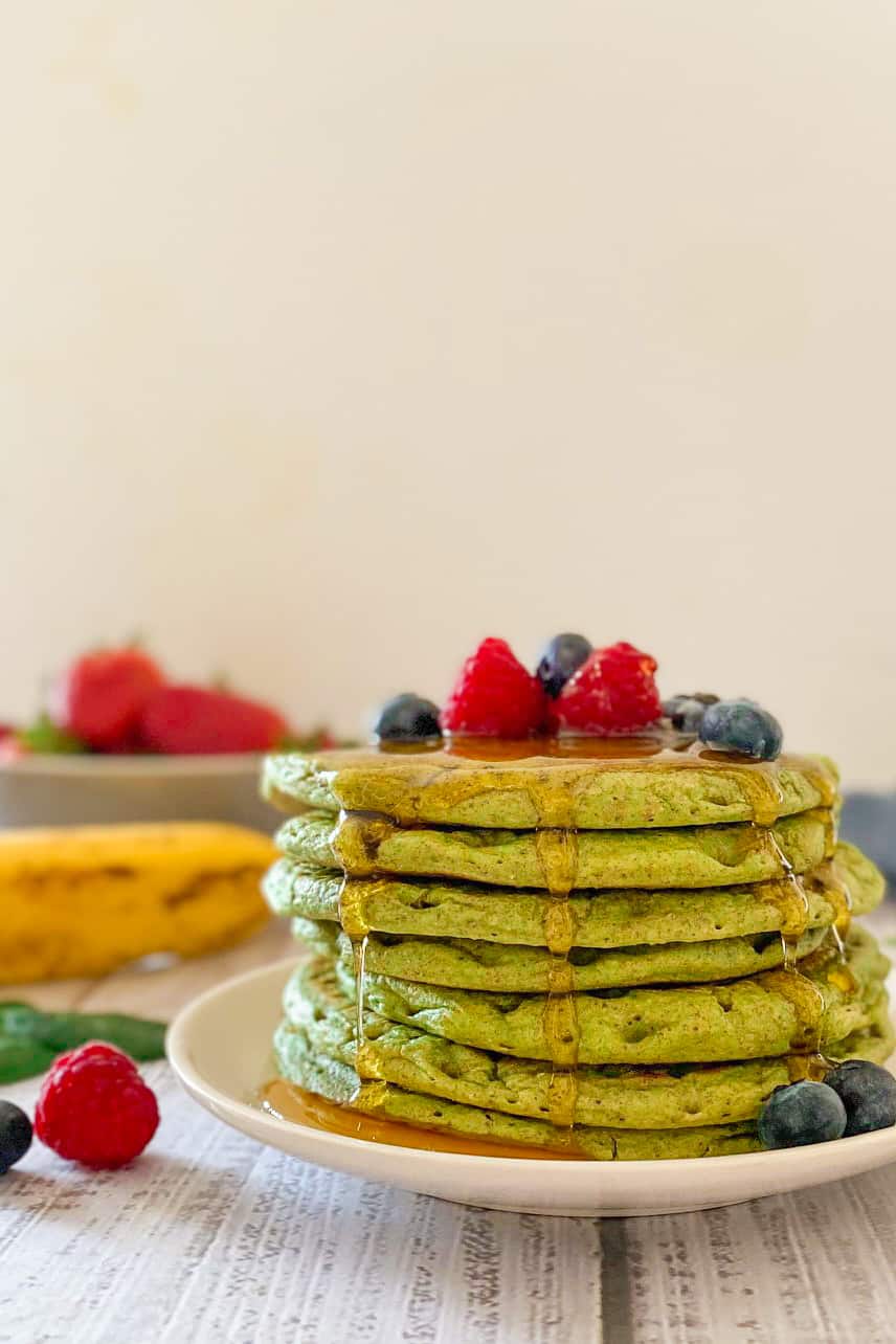 Stack of green pancakes on plate with berries on top.