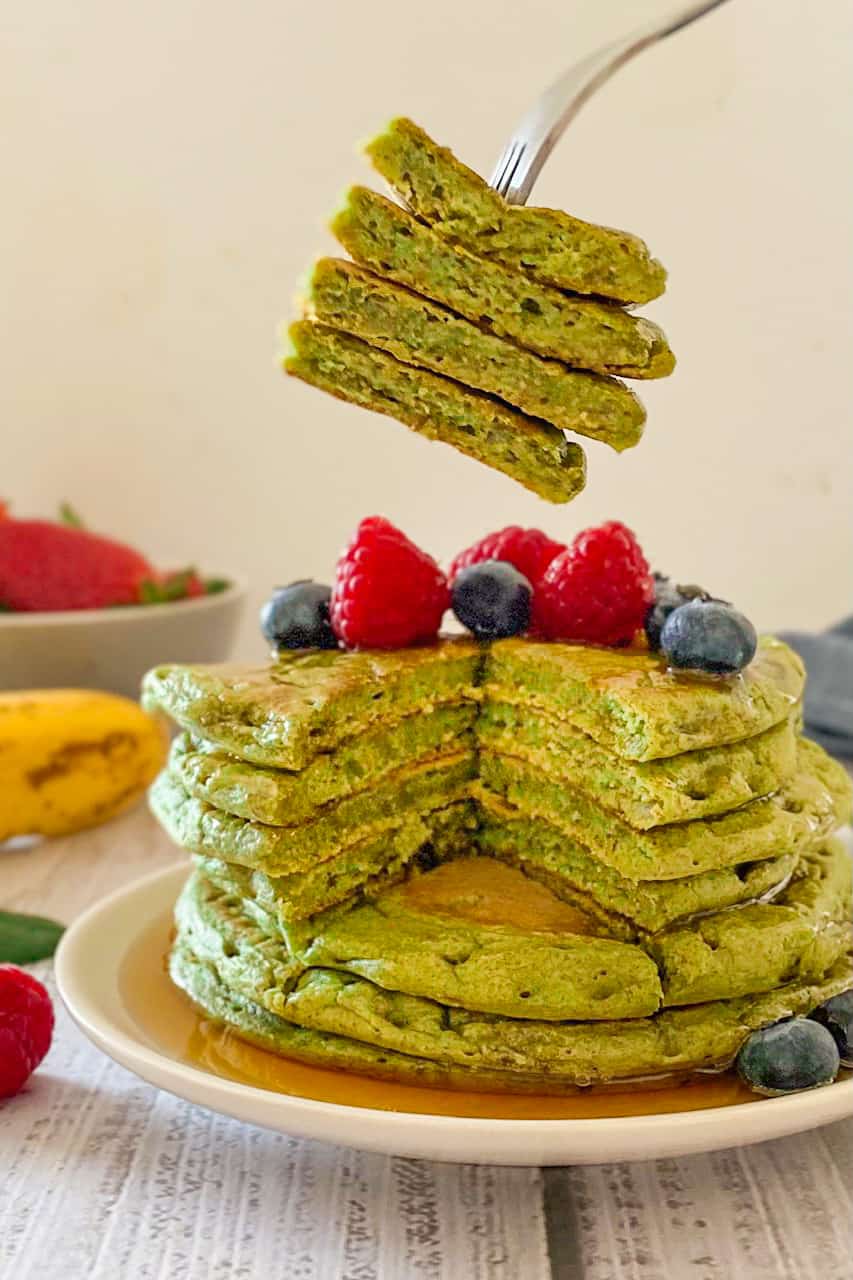 Stack of green pancakes with fork holding up triangular pancake wedge.