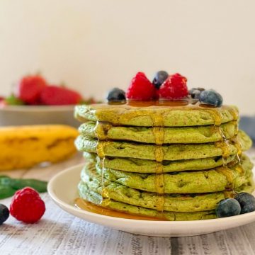 Stack of green pancakes on plate with berries on top.