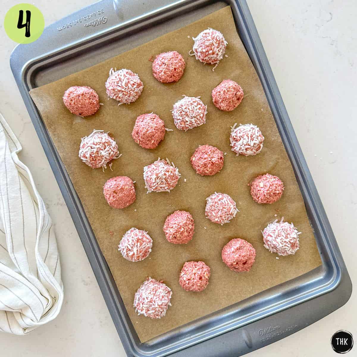 Strawberry bliss balls on a baking sheet with half of them coated in coconut shreds.