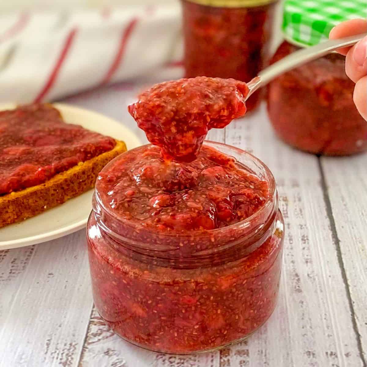 Spoonful of strawberry jam being held above the jar.