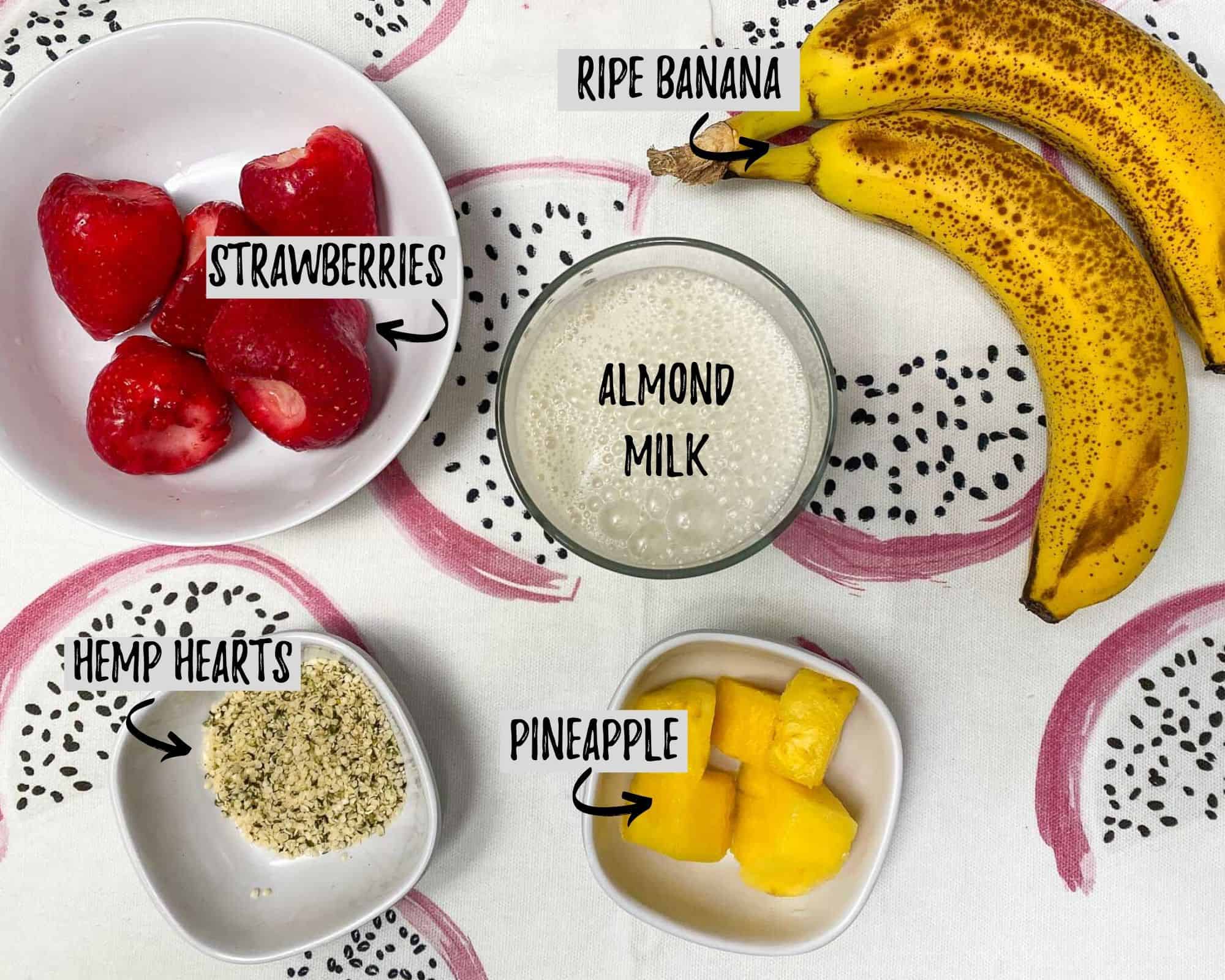 banana, bowl of strawberries, bowl of pineapple, glass of milk, and small bowl of hemp hearts