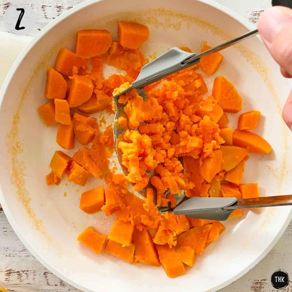 Potato masher mashing cubed and cooked sweet potato.