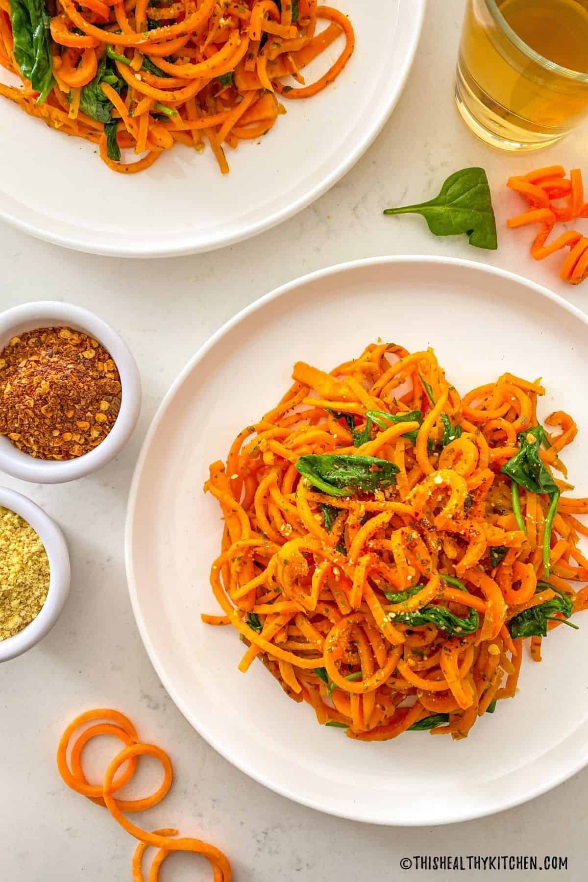 Plate of sweet potato noodles with wilted spinach and chili flakes on top.