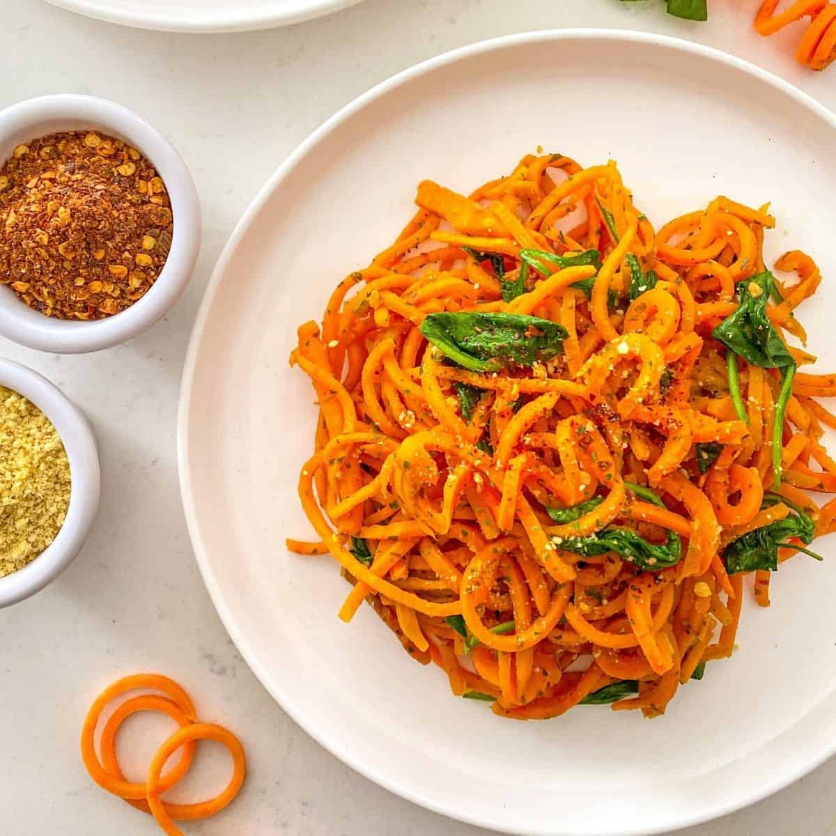 Plate of sweet potato noodles with wilted spinach and chili flakes on top.