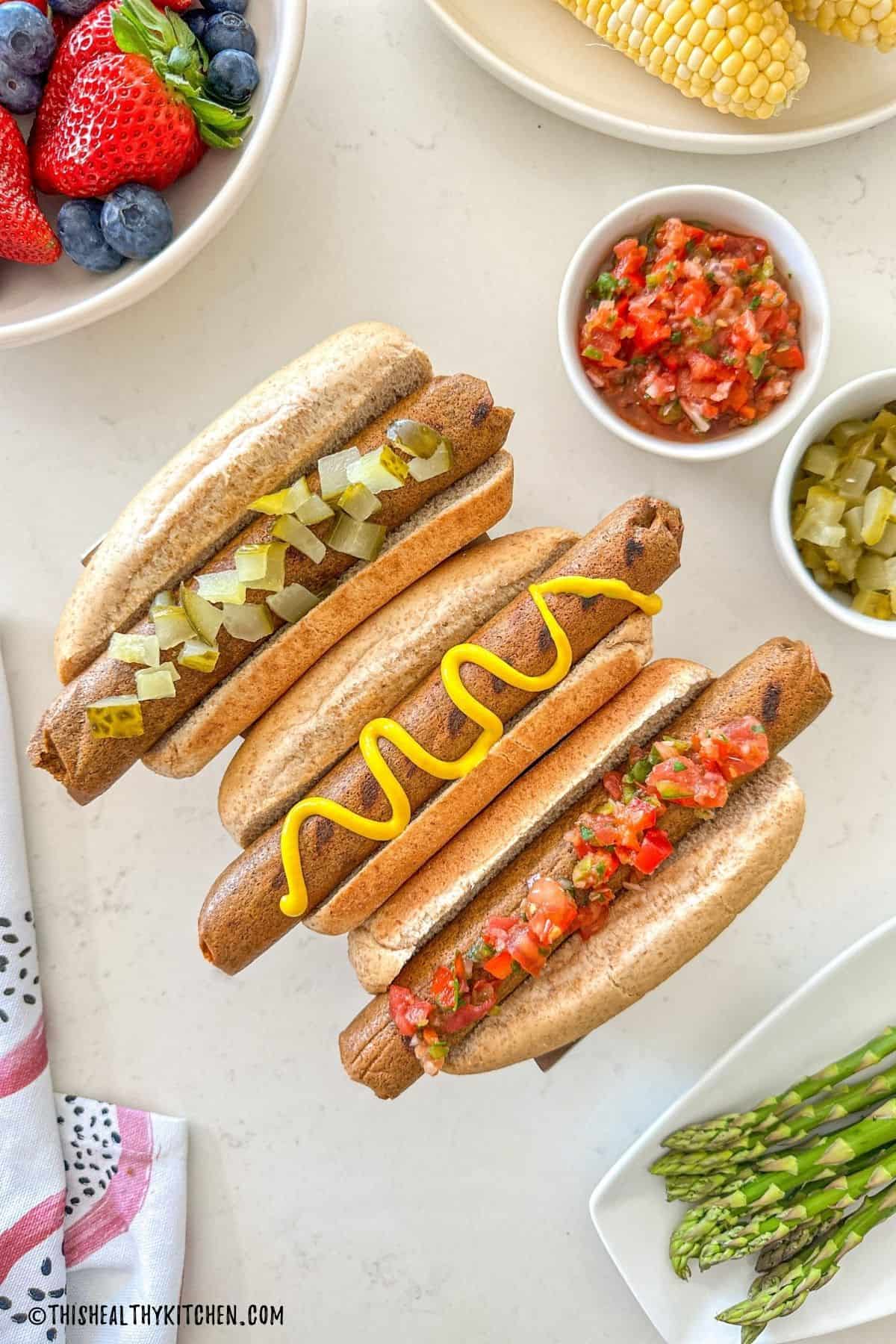 Three tofu hot dogs in buns with toppings.