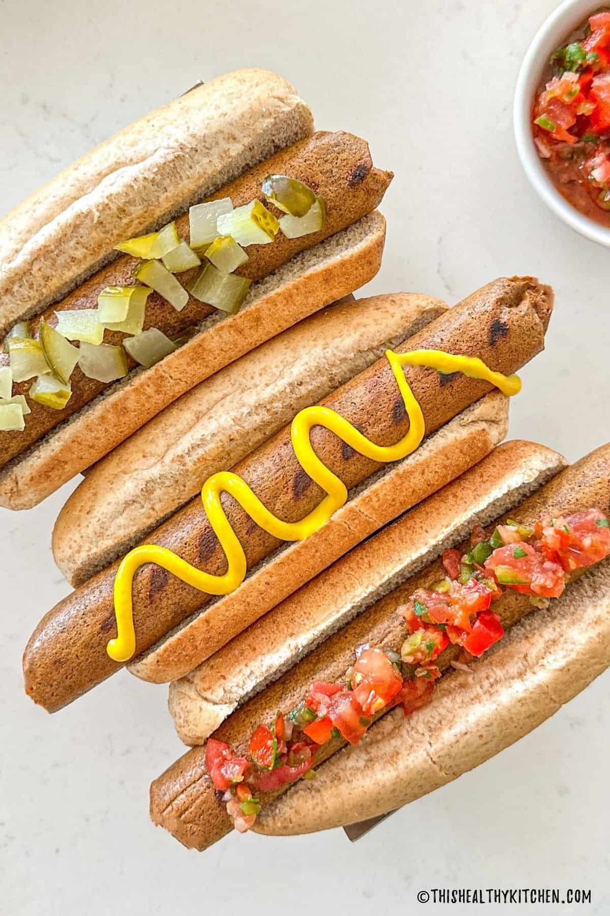 Three tofu hot dogs in buns with toppings.