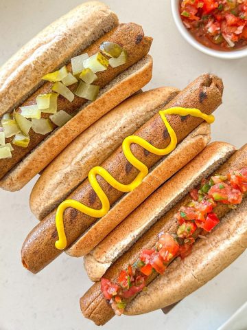 Three tofu hot dogs in buns with toppings.