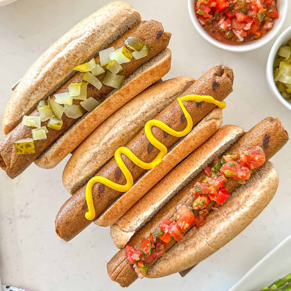Three tofu hot dogs in buns with toppings.