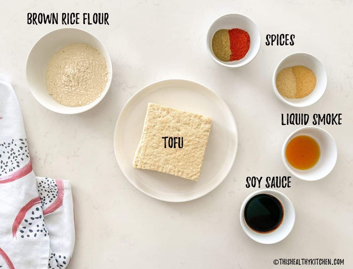 Plate with tofu, bowl of rice flour, and small prep bowls of spices and seasonings on countertop.
