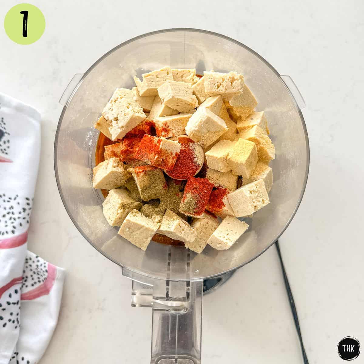 Cubed tofu in food processor with seasonings on top.