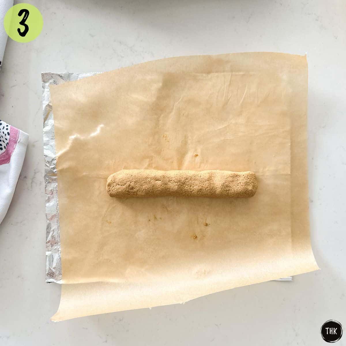 Tofu hot dogs being shaped into logs over a sheet of parchment paper.