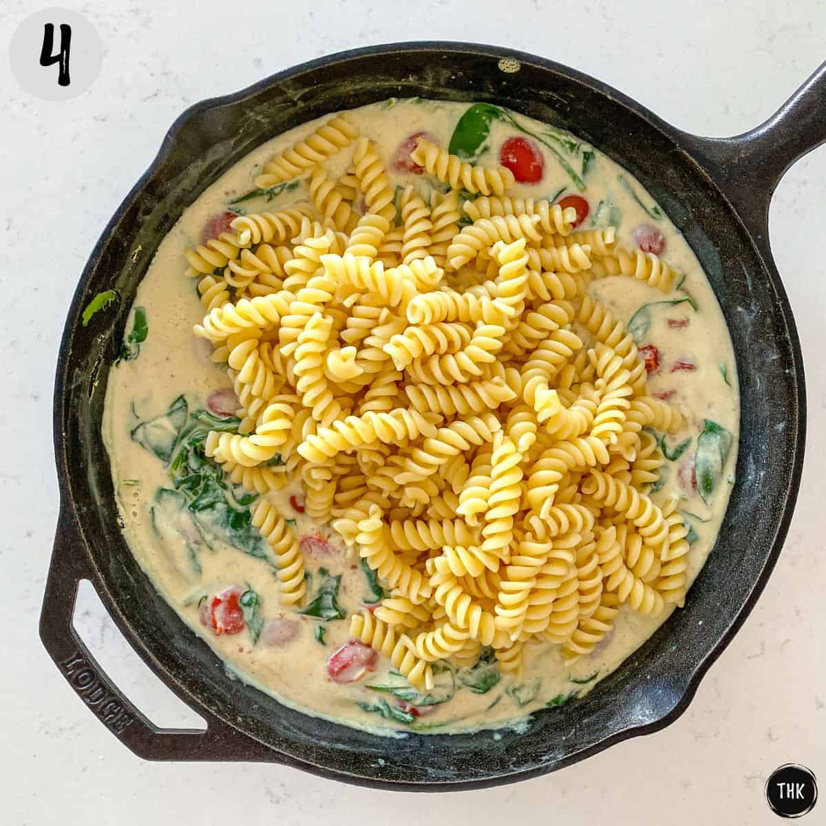 White tofu pasta sauce in skillet with cooked pasta on top.