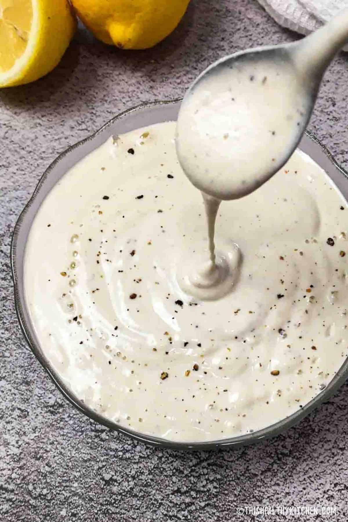 Vegan alfredo sauce in glass bowl with spoon of sauce dripping into bowl.