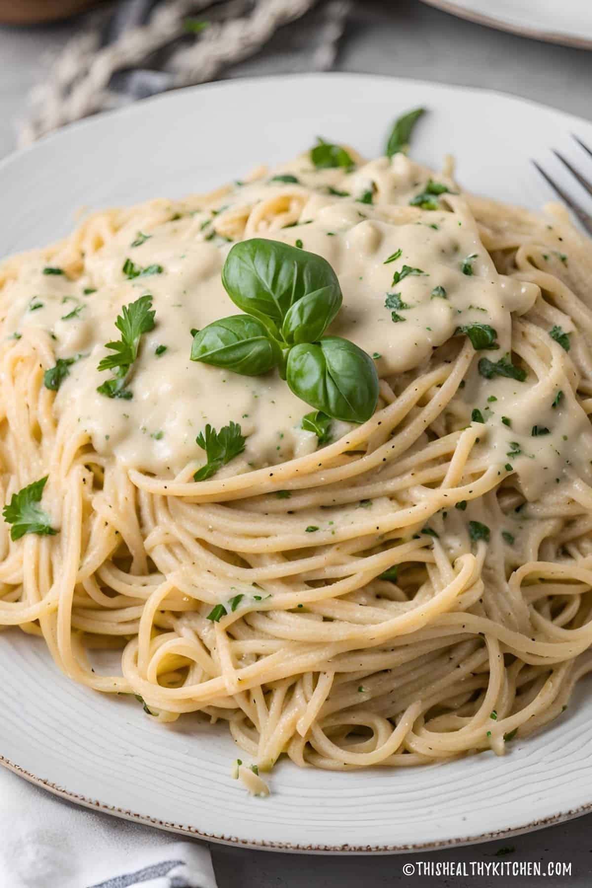 Plate of spaghetti with vegan alfredo sauce and fresh basil on top.