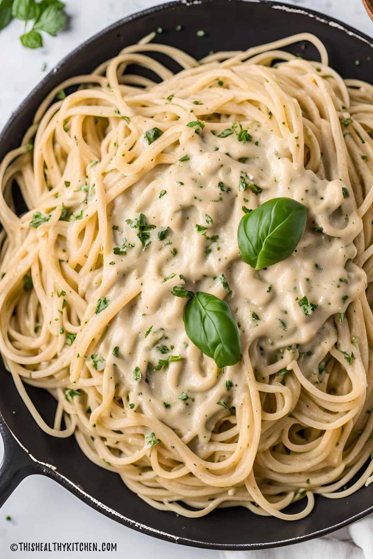 Vegan alfredo sauce spaghetti inside cast iron pan.