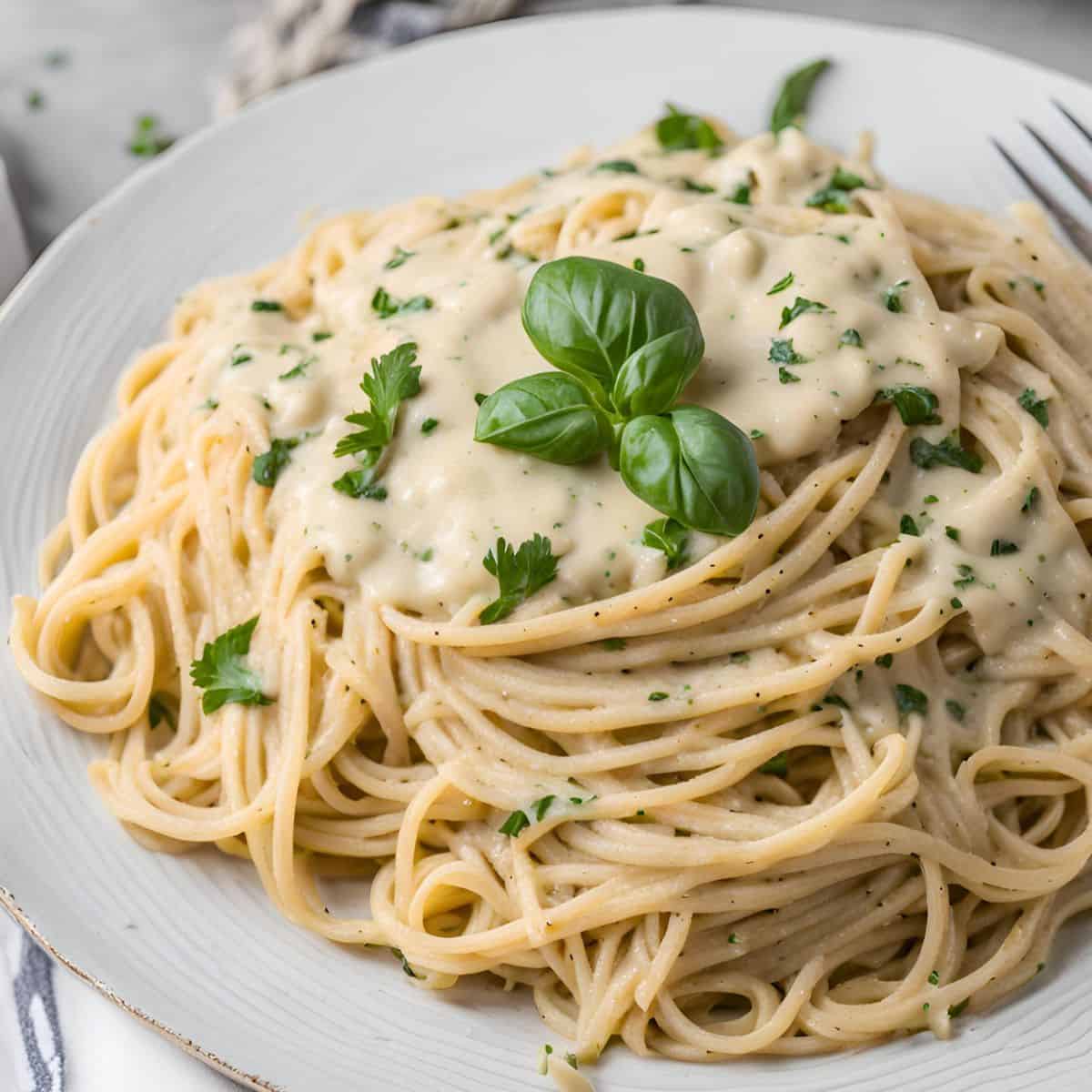 Plate of spaghetti with vegan alfredo sauce and fresh basil on top.