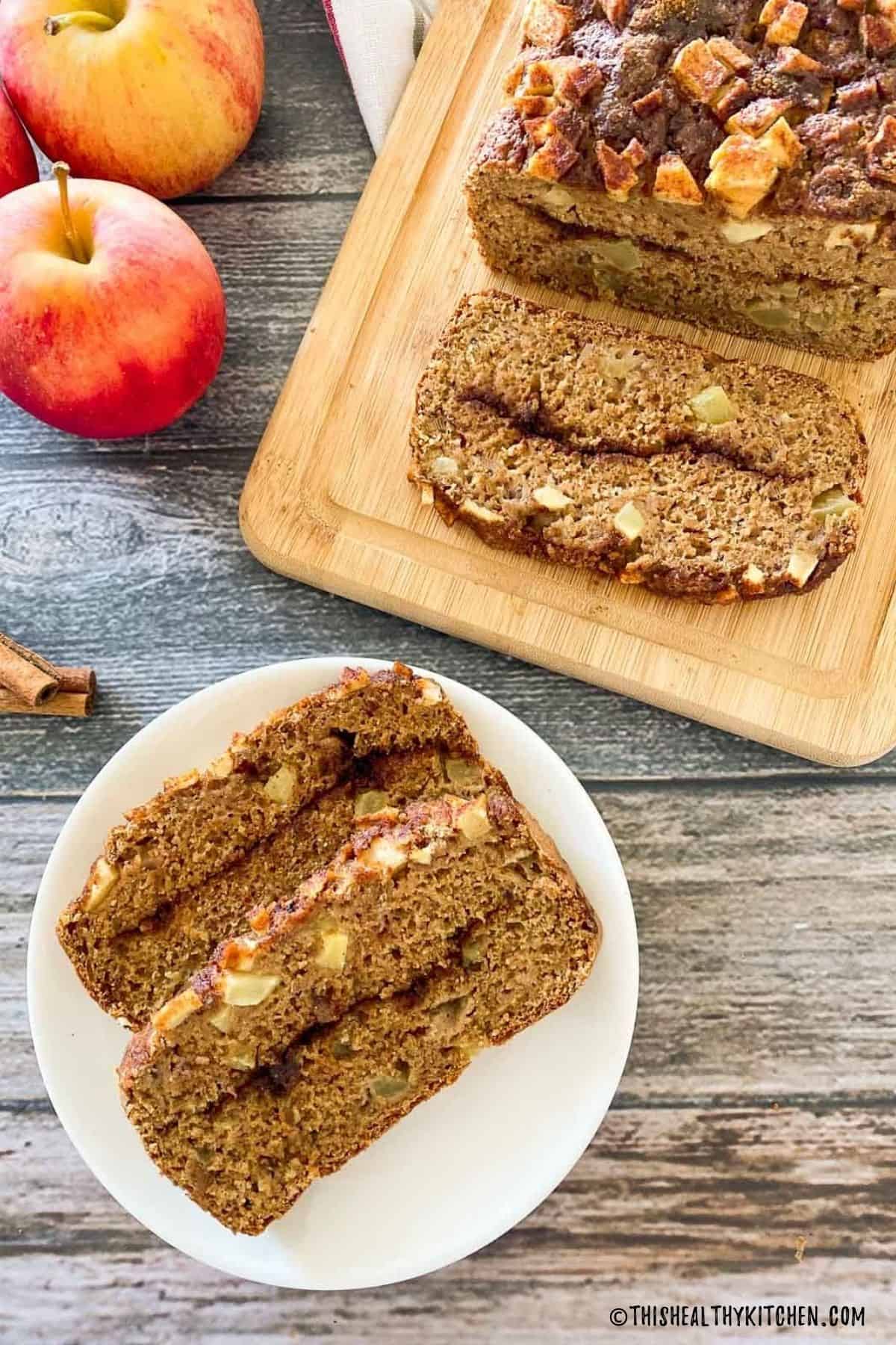 Two slices of apple bread on white plate with remaining loaf on cutting board.