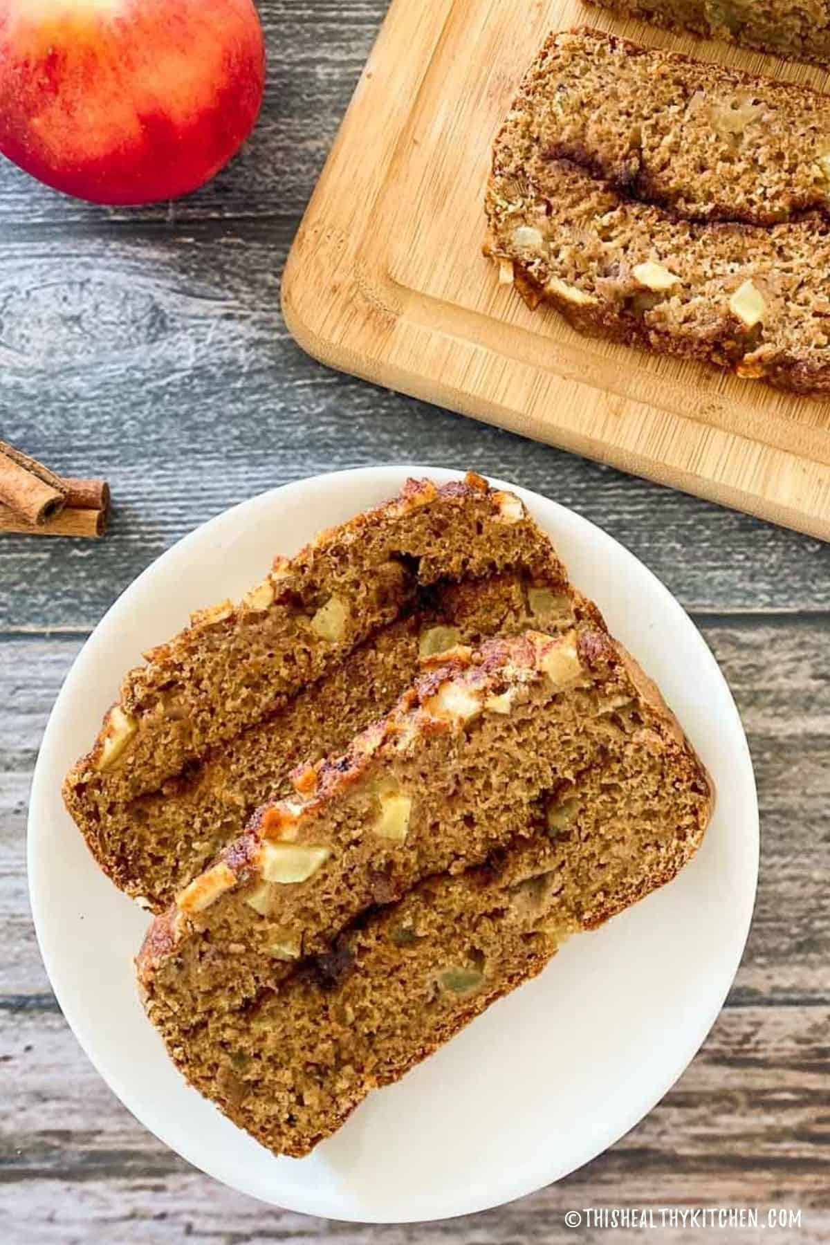 Two slices of apple bread on white plate with remaining loaf on cutting board.