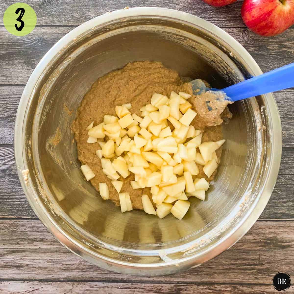 Cake batter in mixing bowl with diced apples on top.