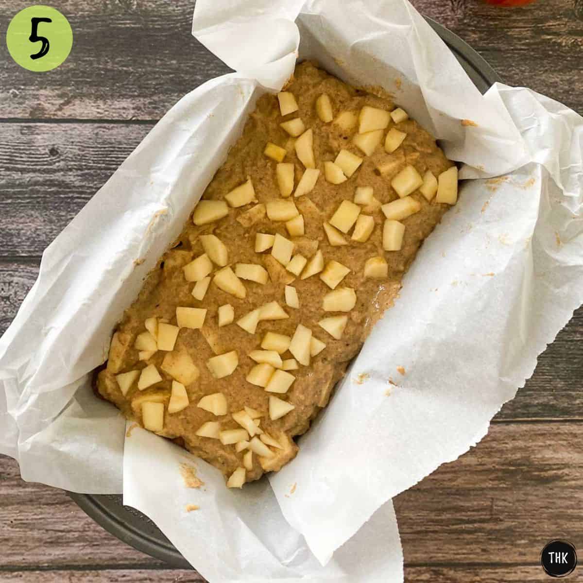 Unbaked apple bread inside loaf pan lined with parchment paper.