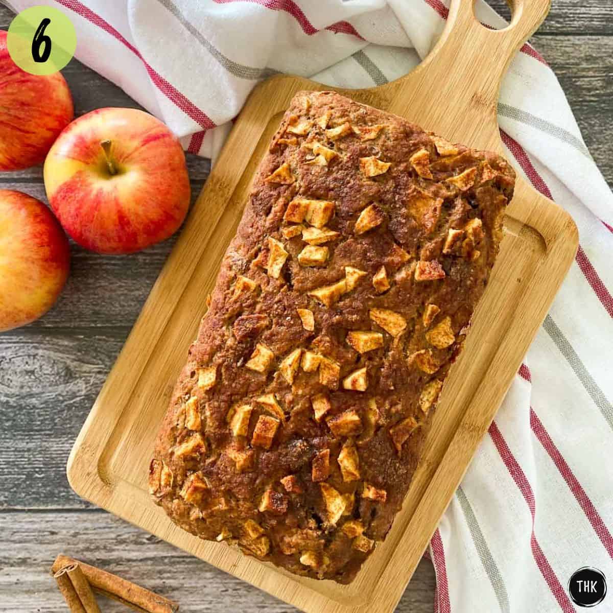 Baked apple bread resting on cutting board with apples beside it.