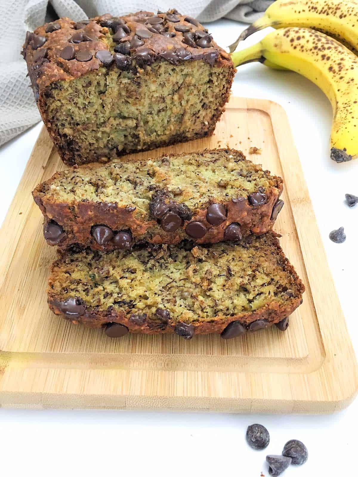 Vegan banana bread on cutting board with two slices  laying on top of one another.