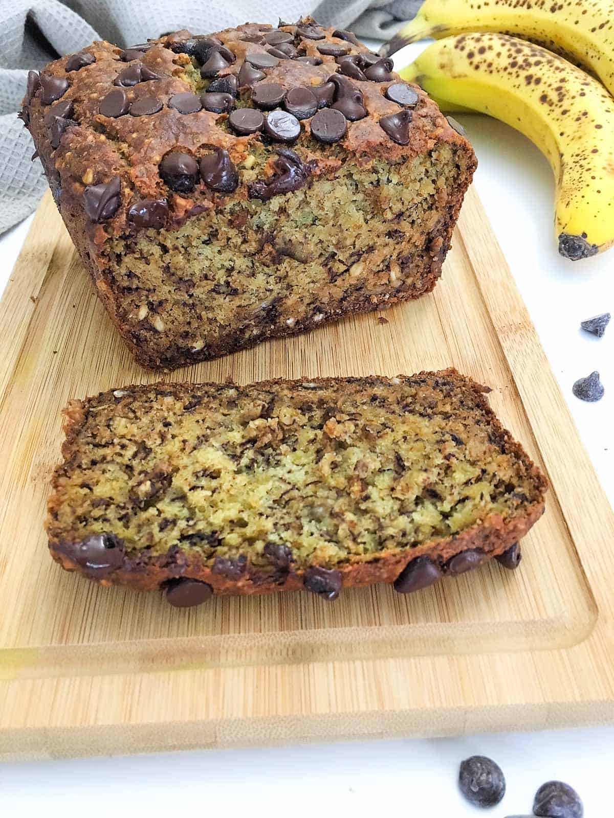 Banana bread with chocolate chips on top on wooden cutting board with one slice cut.
