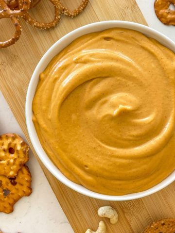 White bowl with orange dip inside and crackers and pretzels scattered around it.