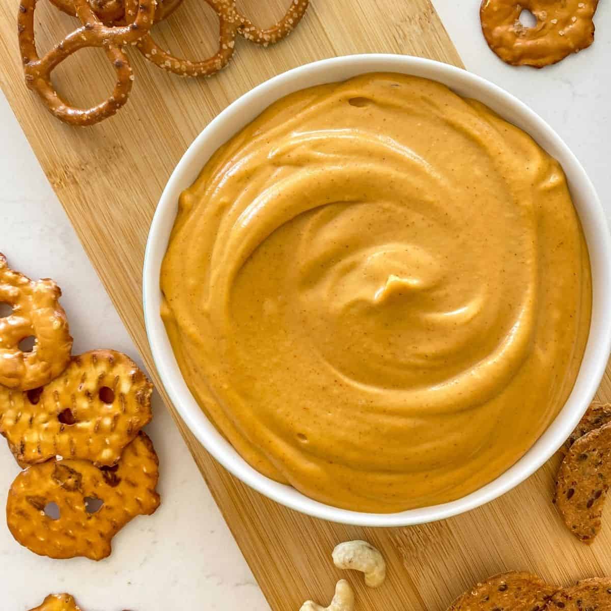White bowl with orange dip inside and crackers and pretzels scattered around it.
