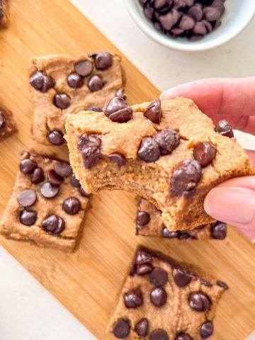 Hand holding up a white bean blondie with a bite taken from it.