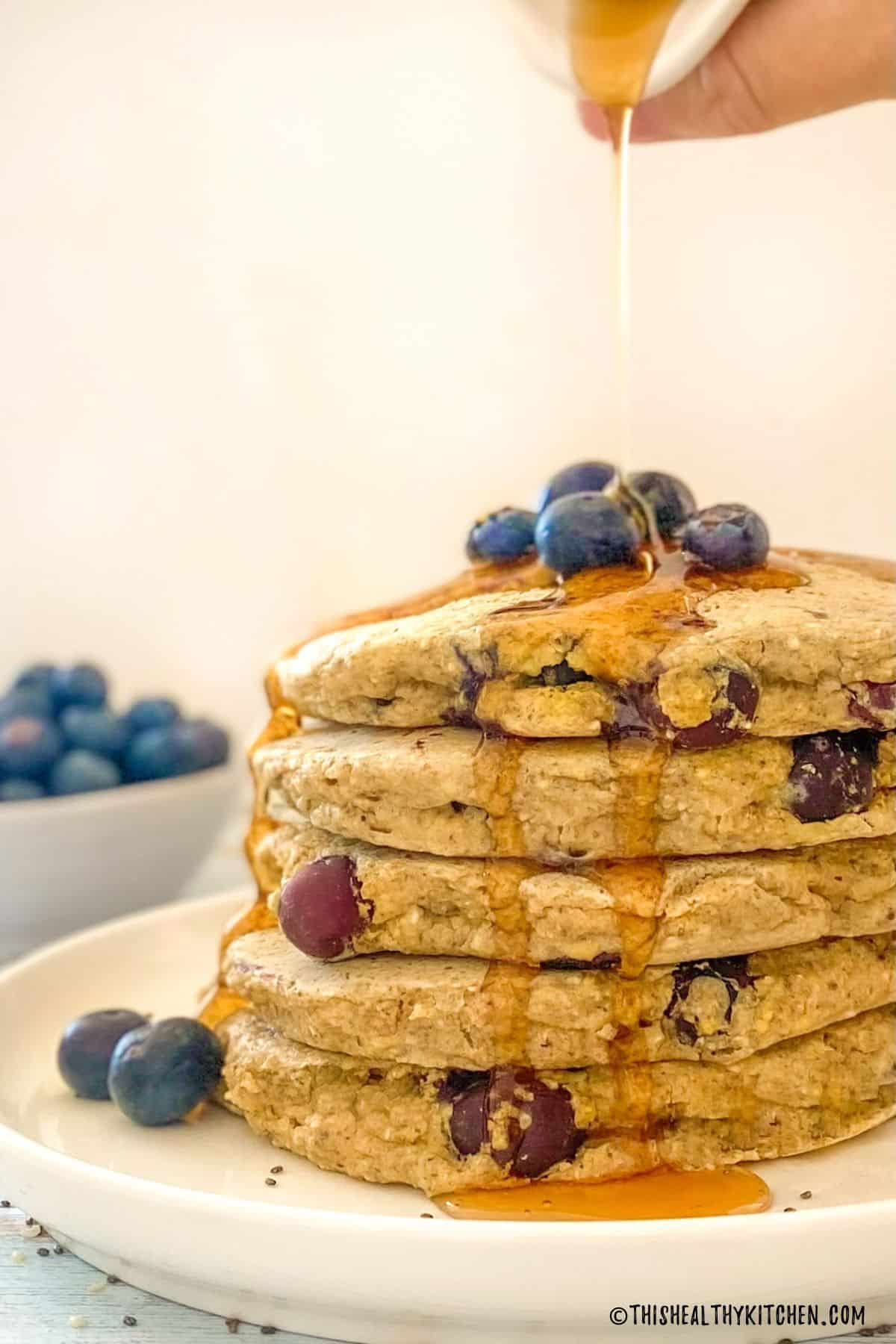Syrup being poured over stack of blueberry pancakes.