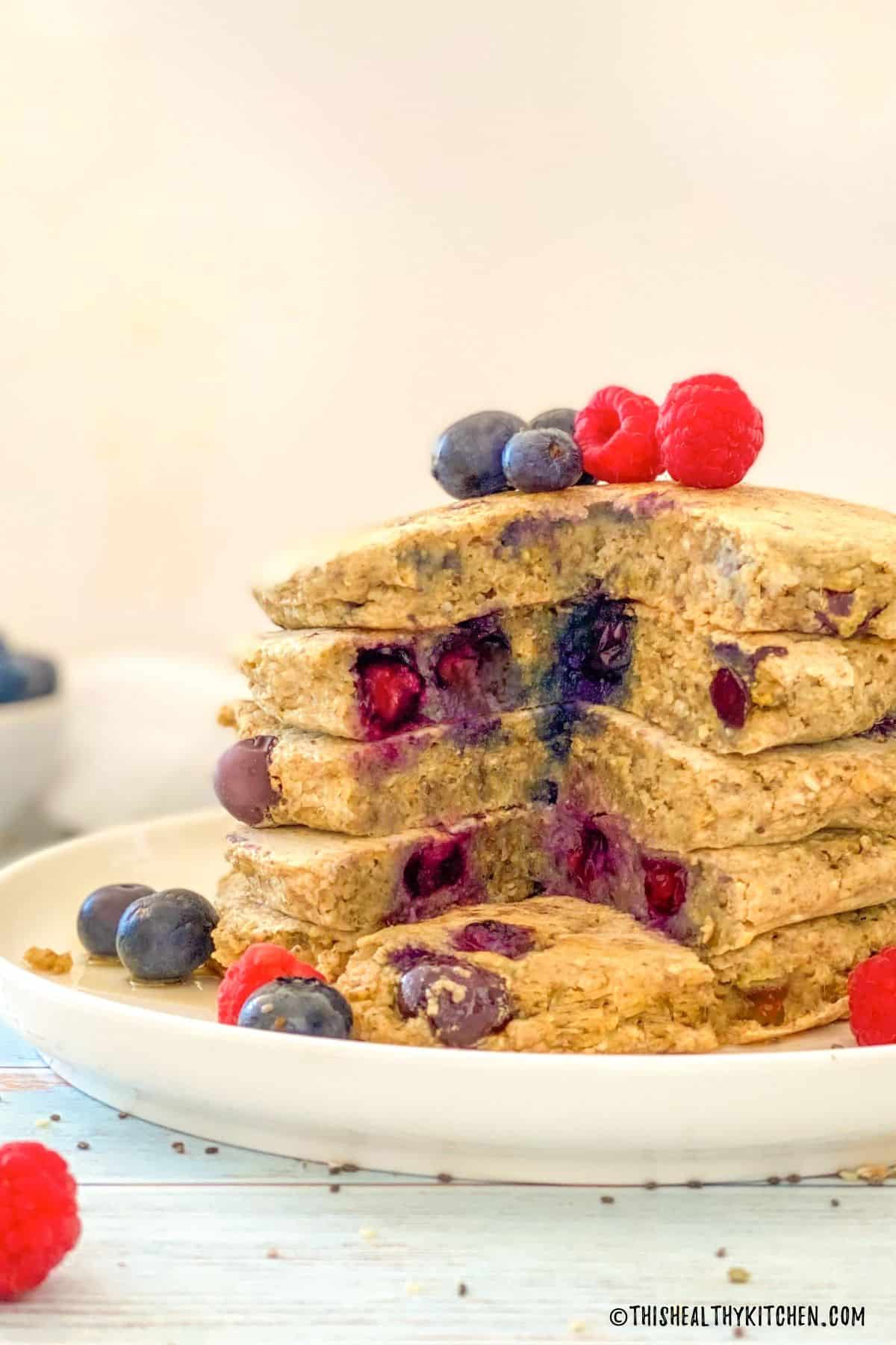 Triangular cut out through stack of pancakes with blueberries and raspberries on top.